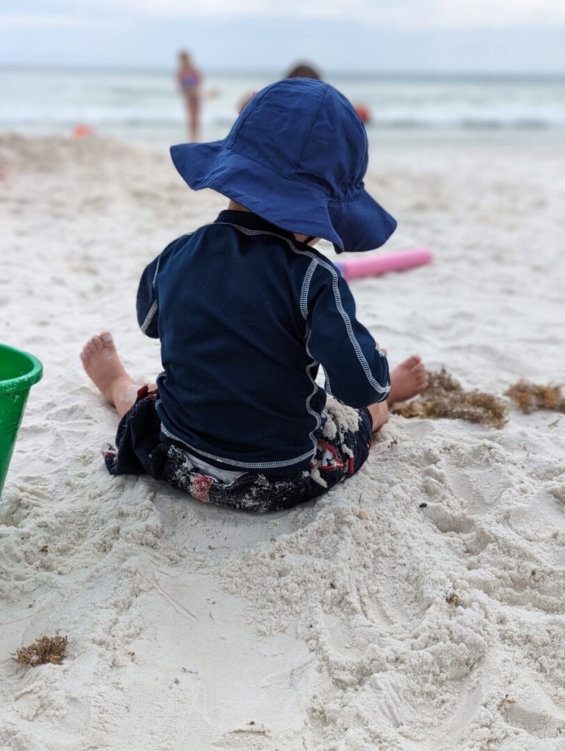 A child sitting on the beach in front of some sand.