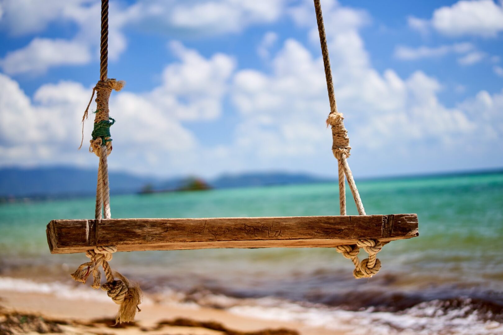 A swing on the beach with water in background.
